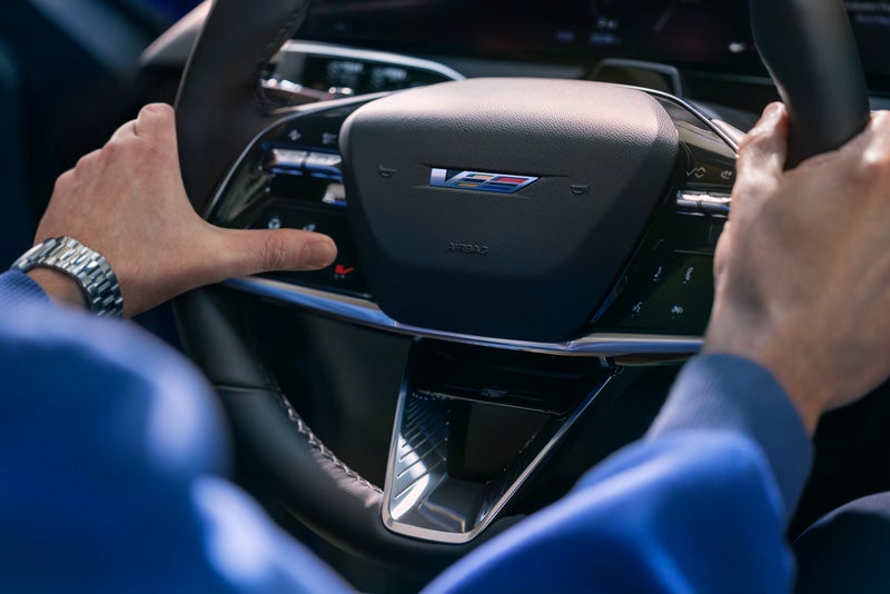 Close-up of a Man About to Press the V-Button on the 2026 OPTIQ-V Steering Wheel | Cole Valley Cadillac in Warren OH